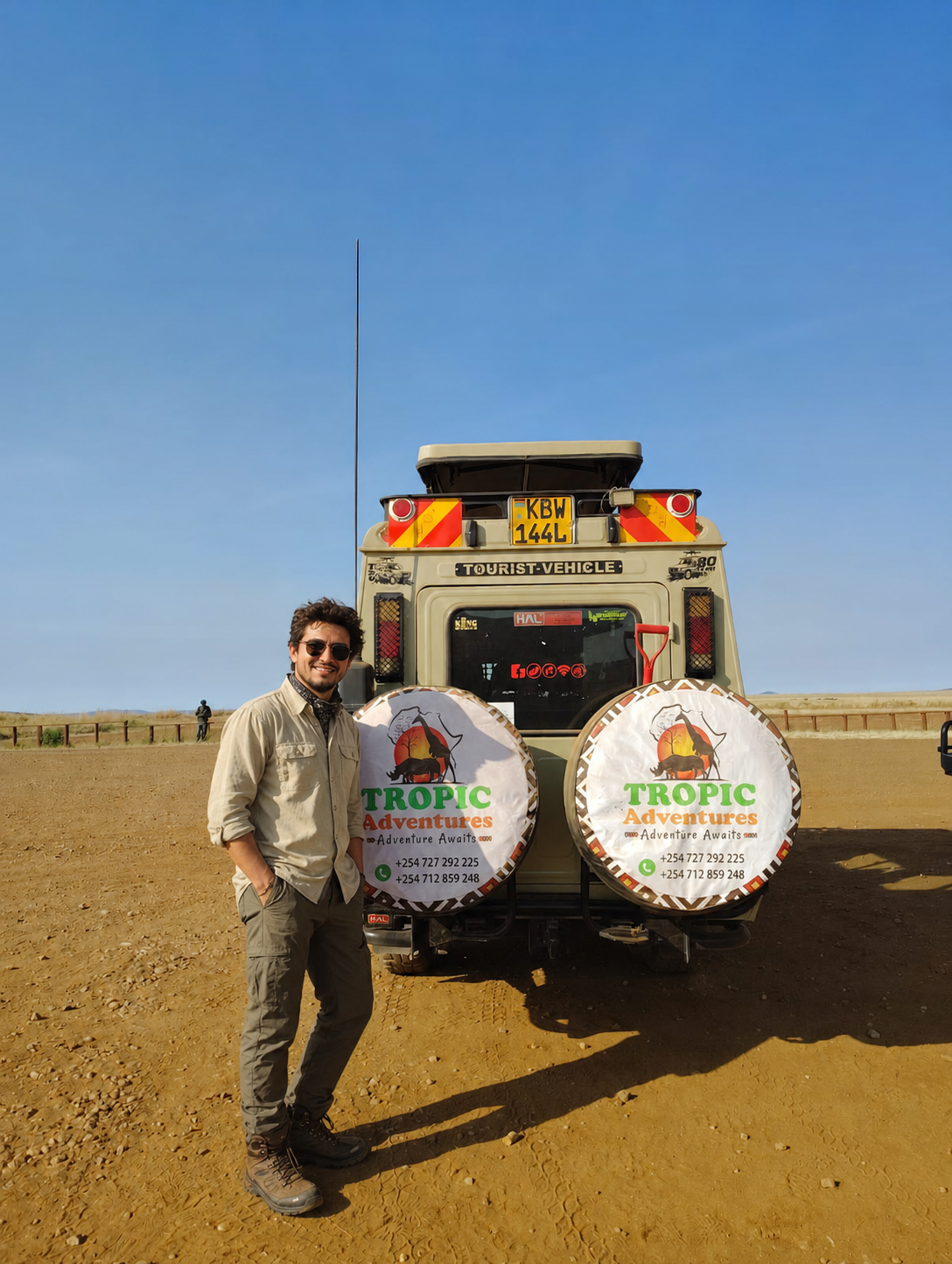 A fictional safari traveler standing beside a Tropic Adventures vehicle in the open plains